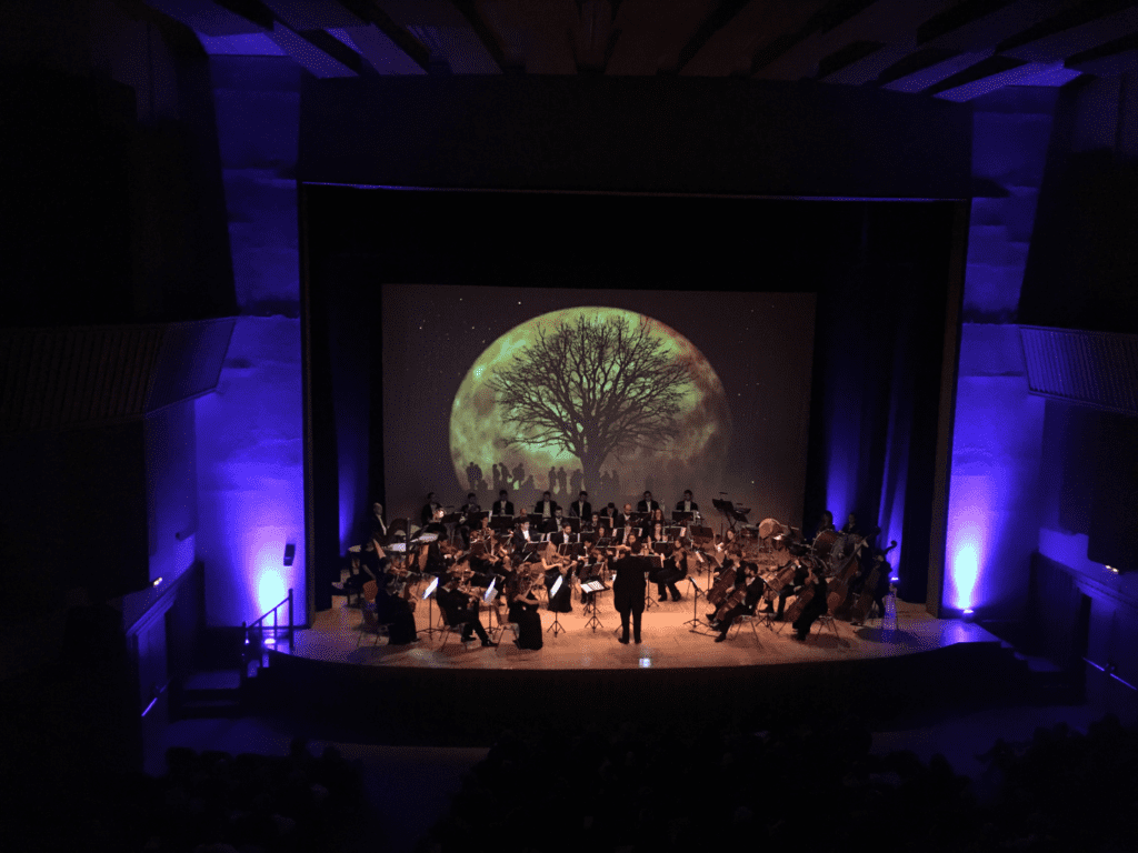 Concierto realizado por la productora audiovisual Kion Eventos en el Auditorio del Palacete de los Duque de Pastrana. Es un concierto con una orquesta sinfónica que están tocando en un escenario y sobre el fondo de una proyección audiovisual. Todo el evento está realizado por técnicos de video y técnicos de sonido.